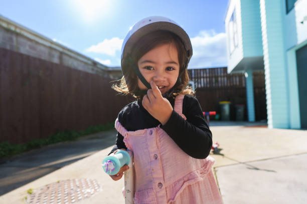 Pacific Islander little girl wearing protective helmet riding a push scooter.