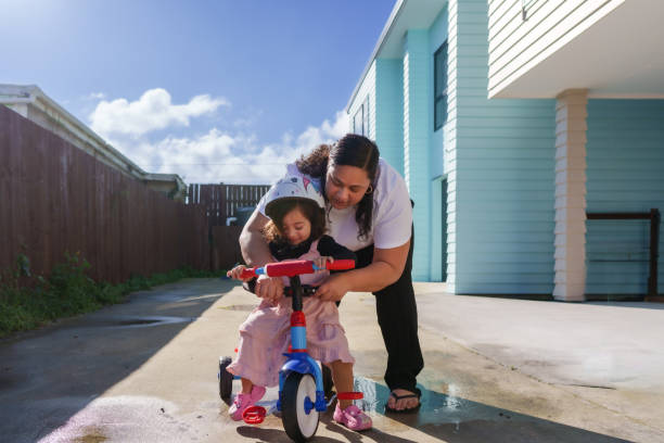 Maori woman guiding her little girl to ride a tricycle at home, mother support for her daughter.