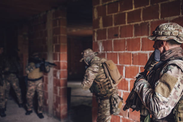 Group of soldiers setting up a tactical position in a dimly lit hallway of an unfinished brick building, showcasing discipline and readiness for a potential engagement situation.