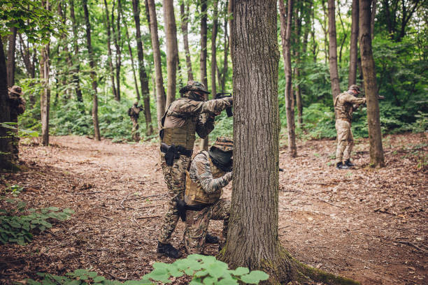 Multiple soldiers in camouflage uniforms are seen positioning themselves strategically around trees, securing the forest area during a military operation, showcasing teamwork and precision.