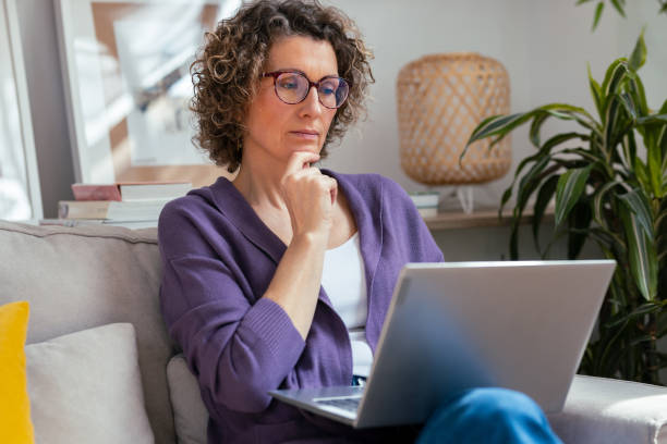 istock Kind mature woman using laptop while relaxing sitting on the couch at home 2163687083