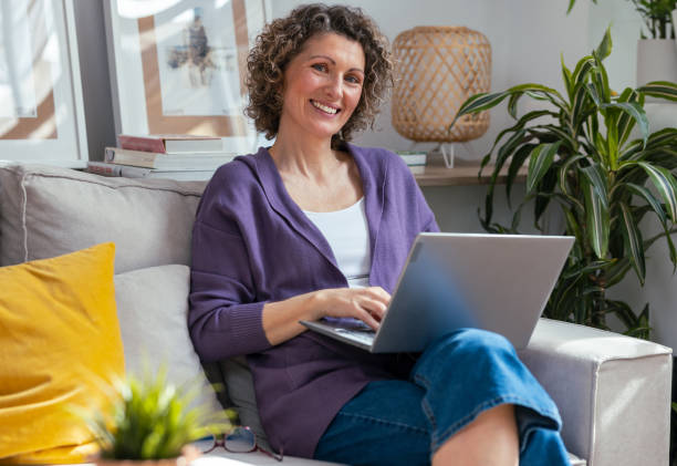 istock Kind mature woman using laptop while relaxing sitting on the couch at home 2163687178
