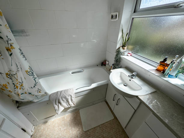 istock Image of domestic bathroom with white bath tub, white tiled wall, waterproof, flower patterned shower curtain, sink with chrome mixer tap in bathroom counter over vanity cabinet, mosaic tiled design vinyl flooring, elevated view 2163688821