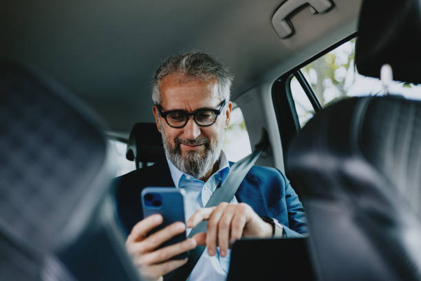 istock Mature Businessman Using Smartphone in Car with Seatbelt On 2163692179