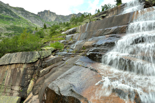 istock A rushing stream of water flows down the stone steps of a natural waterfall surrounded by high mountains on a sunny summer day. 2163707613