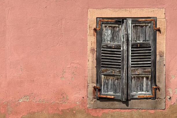 Weathered, wooden, louvered window shutters on a wall, create an interesting European still life scene.