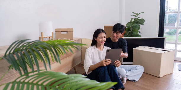 istock Young Couple Moving into New Home, Unpacking Boxes and Using Tablet to Plan Interior Design in Bright Modern Living Room 2163709825