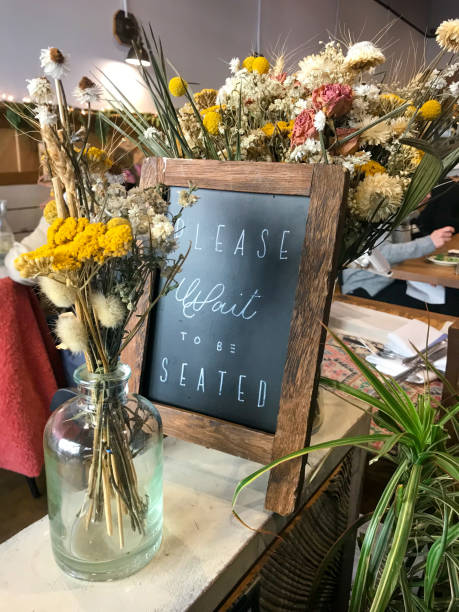 istock Please Wait To Be Seated Sign In Restaurant With Flowers 2163711529