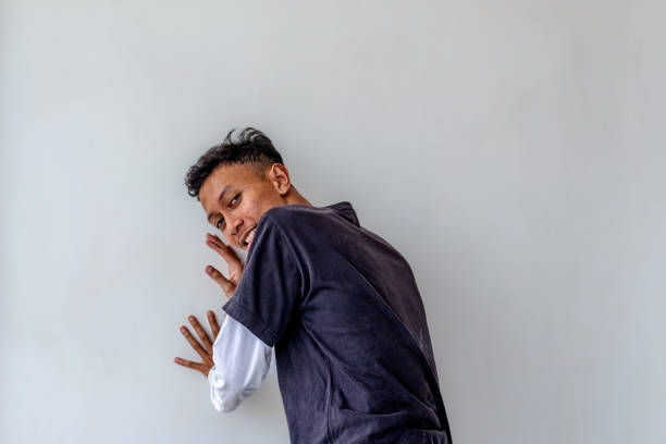 Adult man pushing against a plain white wall while facing away, isolated on a white background. The image captures a dynamic pose, ideal for themes related to strength, effort, and fitness.