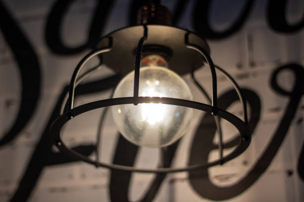 In front of a sign reading save, a light bulb hangs from the ceiling. The scene features keywords such as tints, shades, font, lamp, metal, darkness, and monochrome