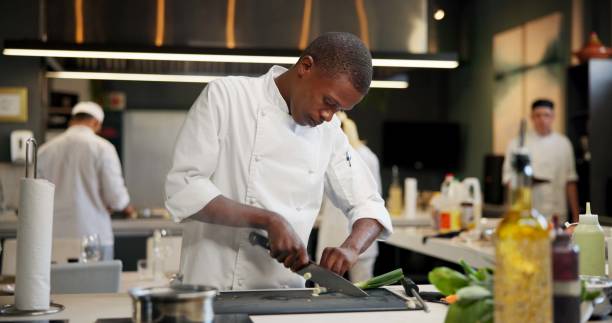 istock Black man, chef and serious with cutting vegetables in kitchen at restaurant for fine dining, meal or creativity. Male employee, professional or cooker with food for culinary, hospitality or catering 2163721170