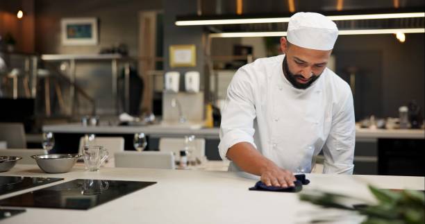 istock Man, chef and serious with cleaning kitchen counter at restaurant for fine dining, meal and creativity. Male employee, professional and cooker with cloth for culinary, hospitality and catering 2163721176