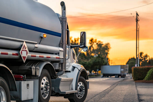 Industrial standard day cab big rig white semi truck transporting flammable liquids in tank semi trailer running on the local road at evening sunset time stock photo