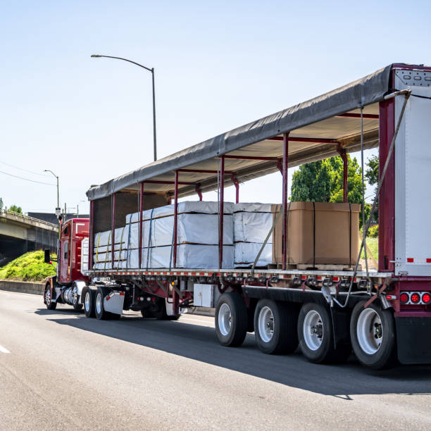 istock Dark red low cab profile big rig semi truck transporting cargo in dry van semi trailer with open Conestoga curtain-side tent walls running on the road 2163722824