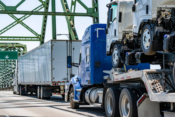 istock Blue big rig semi truck transporting cab over small semi trucks on step deck semi trailer running on the arched truss bridge 2163722859