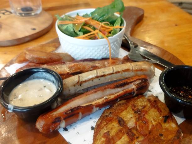 Grilled sausages with mashed potatoes and cherry tomatoes on a wooden table, cutlery nearby. Top view, flat lay.