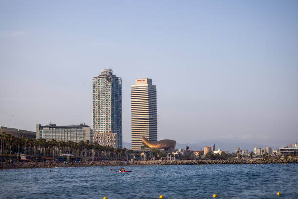 Barcelona, Spain, July 10, 2024 - Skyscrapers overlooking a crowded beachfront in a coastal city under a clear blue sky