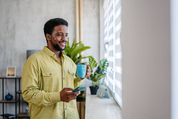 istock Young Man Texting On The Phone While Drinking Coffee By The Window At Home 2163737653