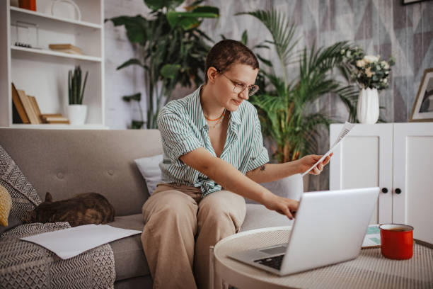 istock Sitter reaching for document next to laptop on sofa 2163740998