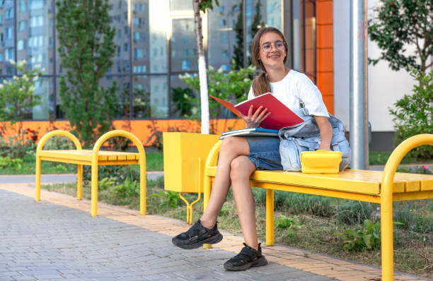 istock The student is sitting on a bench with a lunch box. Student with school supplies. Background school. 2163750881