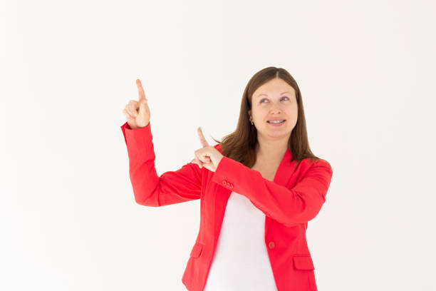 Hey look. Smiling pretty female model pointing fingers left at empty space and inviting to check it out, showing advertisement on white background.
