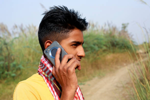 Young men of Indian ethnicity standing on country road outdoor in nature and talking on mobile phone.