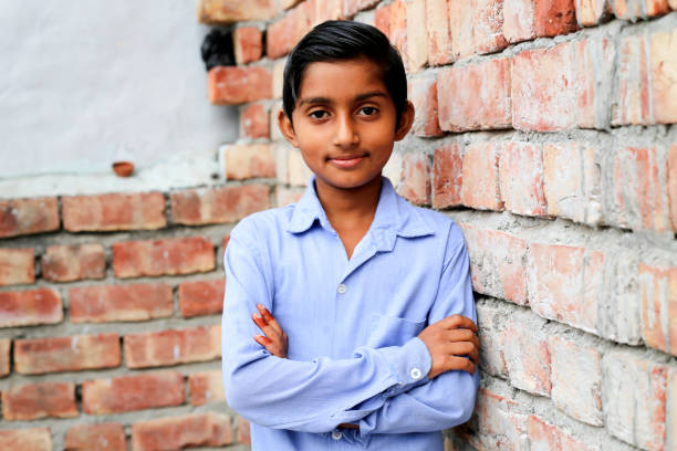 Cheerful elementary age school student of Indian ethnicity standing portrait near brick wall wearing school uniform.