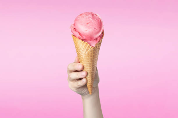 istock Woman's hand holding waffle cone with strawberry ice cream on pink background 2163768804