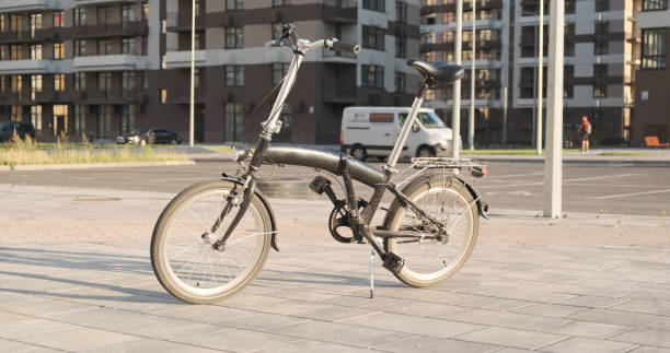 Small folding bicycle on 20 wheels stands lonely on sidewalk in city against backdrop of residential houses. High quality photo