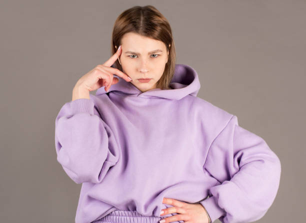 istock Beautiful female with puzzled expression, keeps finger on head, looks aside with bewilderment, poses against gray background. Body language and face expression 2163773272