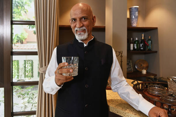 Mature Indian Man Drinking Alcohol Mature Indian man holding glass with alcohol drink and smiling at camera while standing in his house vietnamese old man portrait stock pictures, royalty-free photos & images