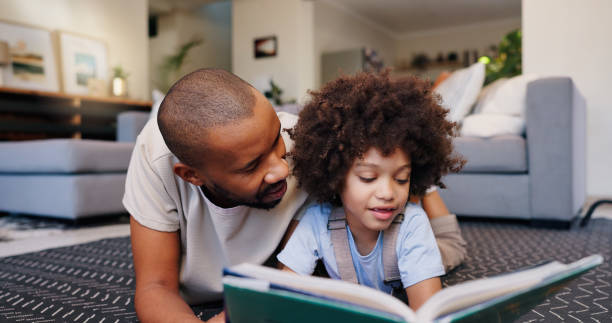istock Reading, dad and child with book on floor for education, learning or language development in living room. Love, African man and girl lying on rug for literacy, storytelling or knowledge in home 2163778135