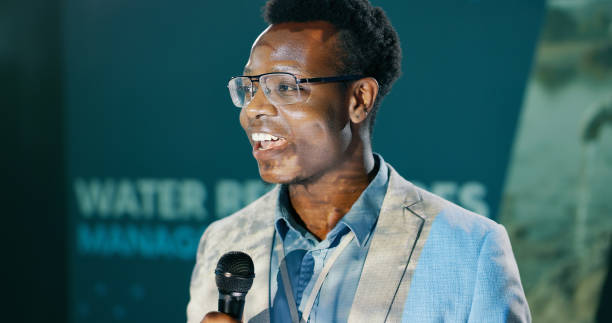 istock Conference, black man and presentation with mic for speech notes, information and convention of water resources. Seminar, male presenter and talk show, audience and public speaking for sustainability 2163778225