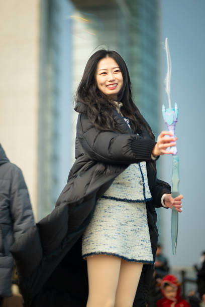 A woman is blowing bubbles outdoors, smiling and enjoying the simple pleasure of the moment. The background is blurred with people, highlighting her joy and focus.