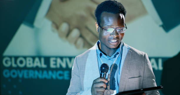istock Presentation, black man and conference with tablet for speech notes, information and discussion of convention. Smile, male presenter and digital education, audience and public speaking for training 2163778236
