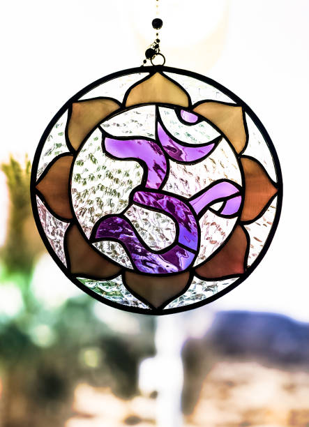 purple and gold stained glass AUM OM symbol glowing in the warm sunlight hanging in a window