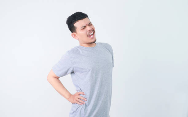 istock A man in a grey shirt bends over slightly and holds his lower back with a pained expression, indicating back pain or discomfort. health and welness concept. 2163799855