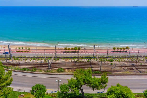 Beachside view featuring railway tracks and clear sea waters in Tarragona, Spain.