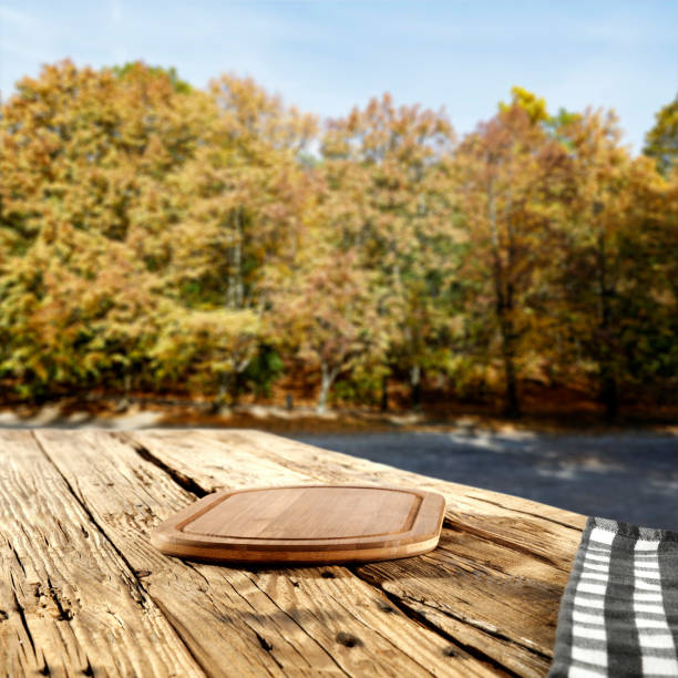 Empty wooden table with copy space for products. Autumn landscape background. Autumn trees in distance.