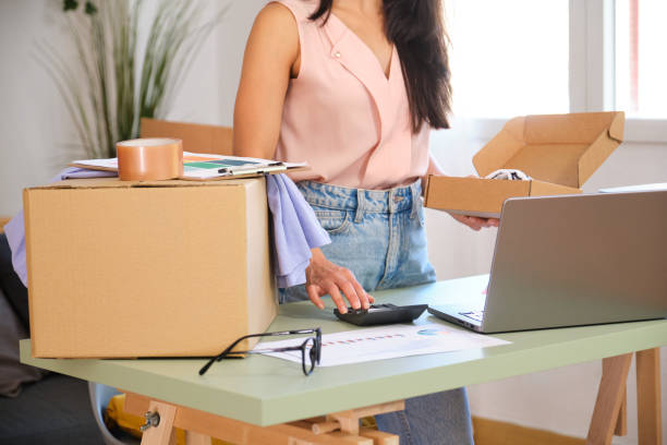 istock Young woman entrepreneur packing a box and using calculator 2163807546