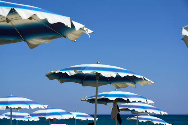 A Blue and white striped beach umbrellas against a clear blue sky on a sunny day