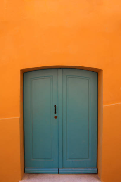 A striking blue door set against a vivid orange wall creates a captivating contrast in this urban architectural photo. The minimalist design and bold color palette highlight the entrance, making it a standout element. The simple yet powerful composition captures the essence of vibrant city life and architectural aesthetics, perfect for adding a pop of color and character to any collection.