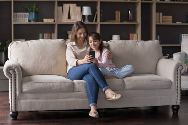 istock Mother and daughter using smartphone in living room 2163842176