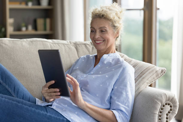 istock Smiling mature female resting on sofa with digital tablet 2163842386