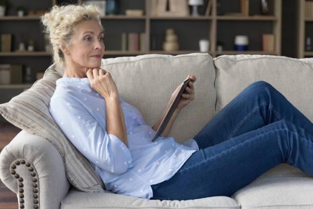 istock Pensive older woman using tablet device seated on comfortable sofa 2163844179