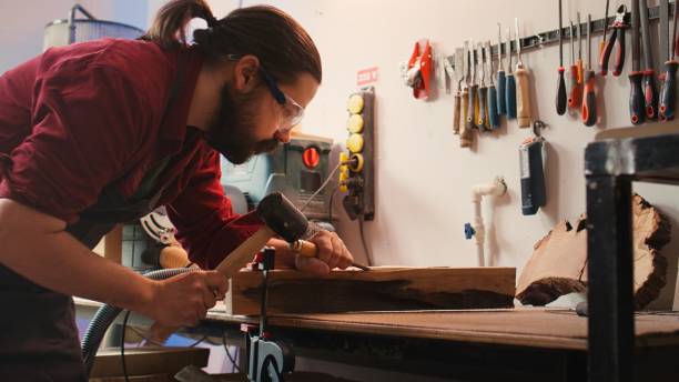 istock Man carves intricate designs into wood using chisel and hammer in carpentry shop 2163846773