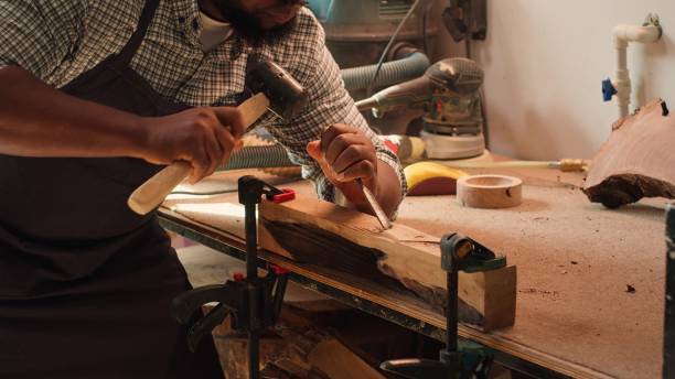 istock Manufacturer shaping raw timber using chisel and hammer, creating wood art 2163847666