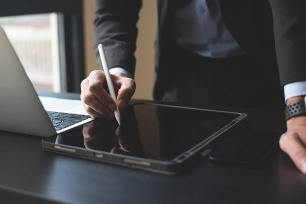 istock Closeup of businessman using stylus pen signing e-document on digital tablet and working on laptop computer. Business man planning work project, proofing digital document on office table, E-signing, electronic signature 2163862386