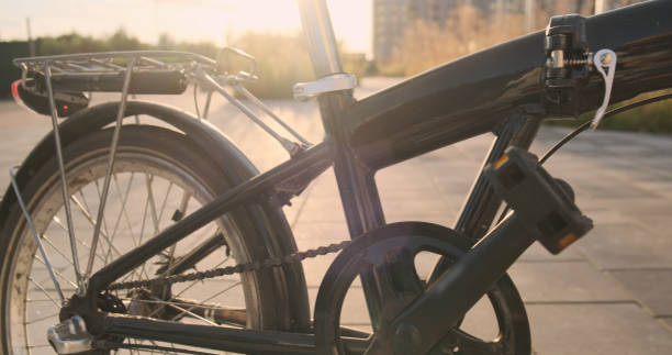 istock Panning side view frame folding bicycle on 20 wheels, close-up, stands on sidewalk in city against backdrop sunset 2163878514