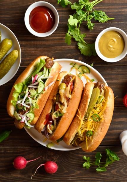 istock Hot dogs loaded with assorted toppings on wooden table 2163897028